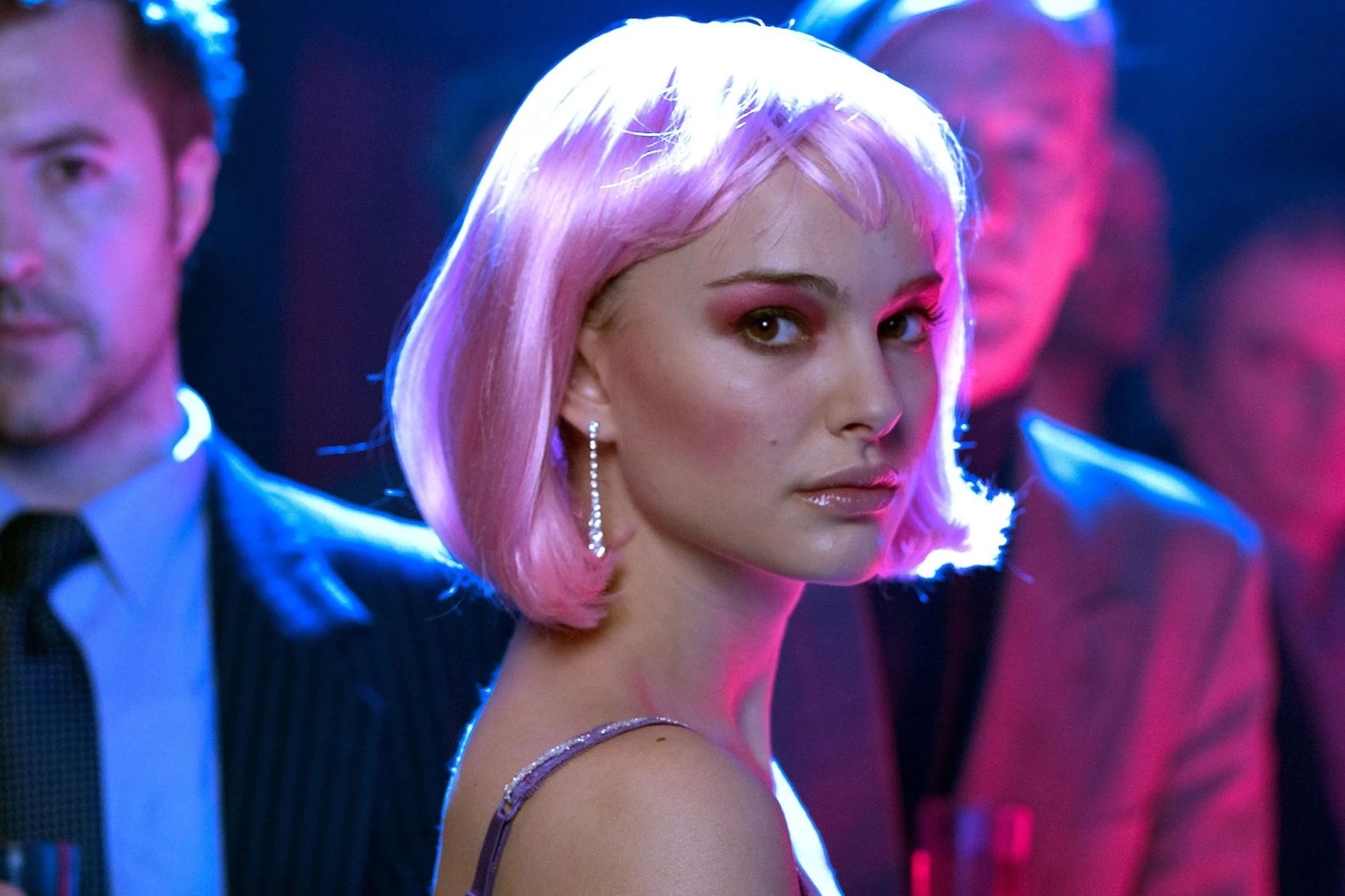 Alice, personagem interpretada por Natalie Portman, com uma peruca curta rosa, e homens aparecendo desfocados ao fundo da cena cena do filme Closer. 