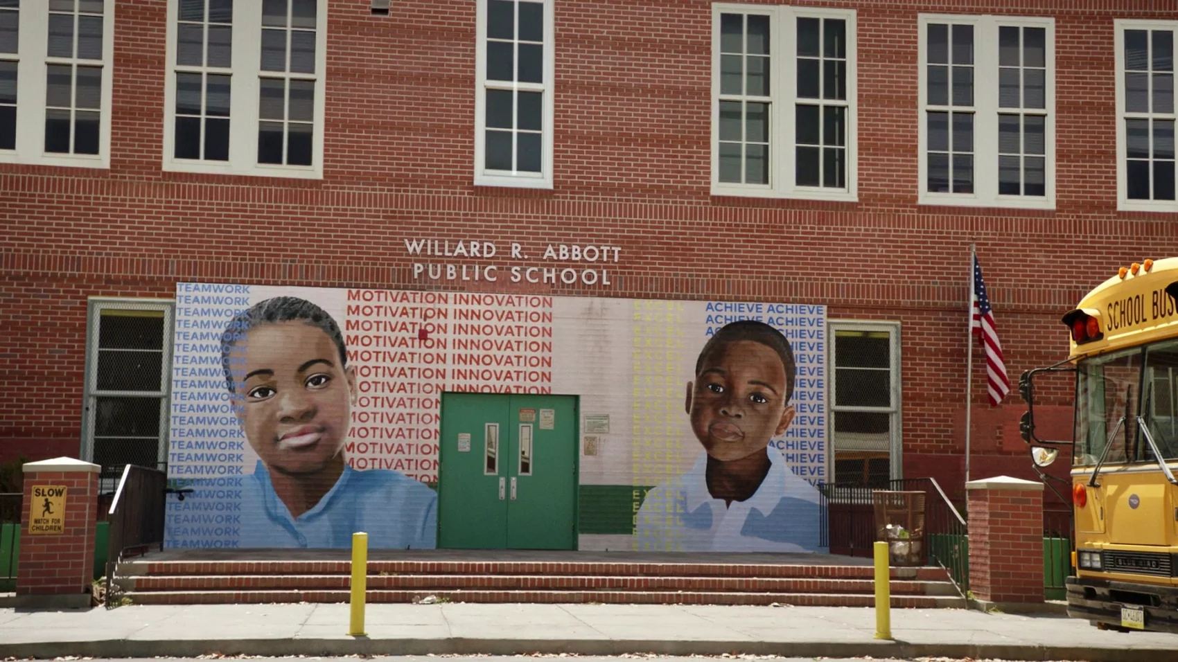 Muro da escola Abbott Elementary. É uma parede de tijolos que possui uma porta verde e um mural onde se vê o desenho de dois estudantes negros. Lê-se "Willard R. Abbott Public School". 
