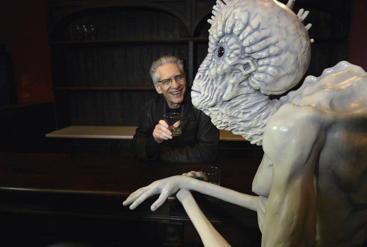 David Cronenberg sentado e segurando um copo com bebida durante a exibição do seu trabalho em Toronto.