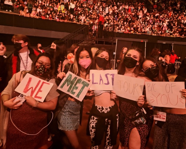 Amigas segurando cartazes com os dizeres "Nos conhecemos na última turnê por sua causa" em Los Angeles, em 2021. (Love on Tour)