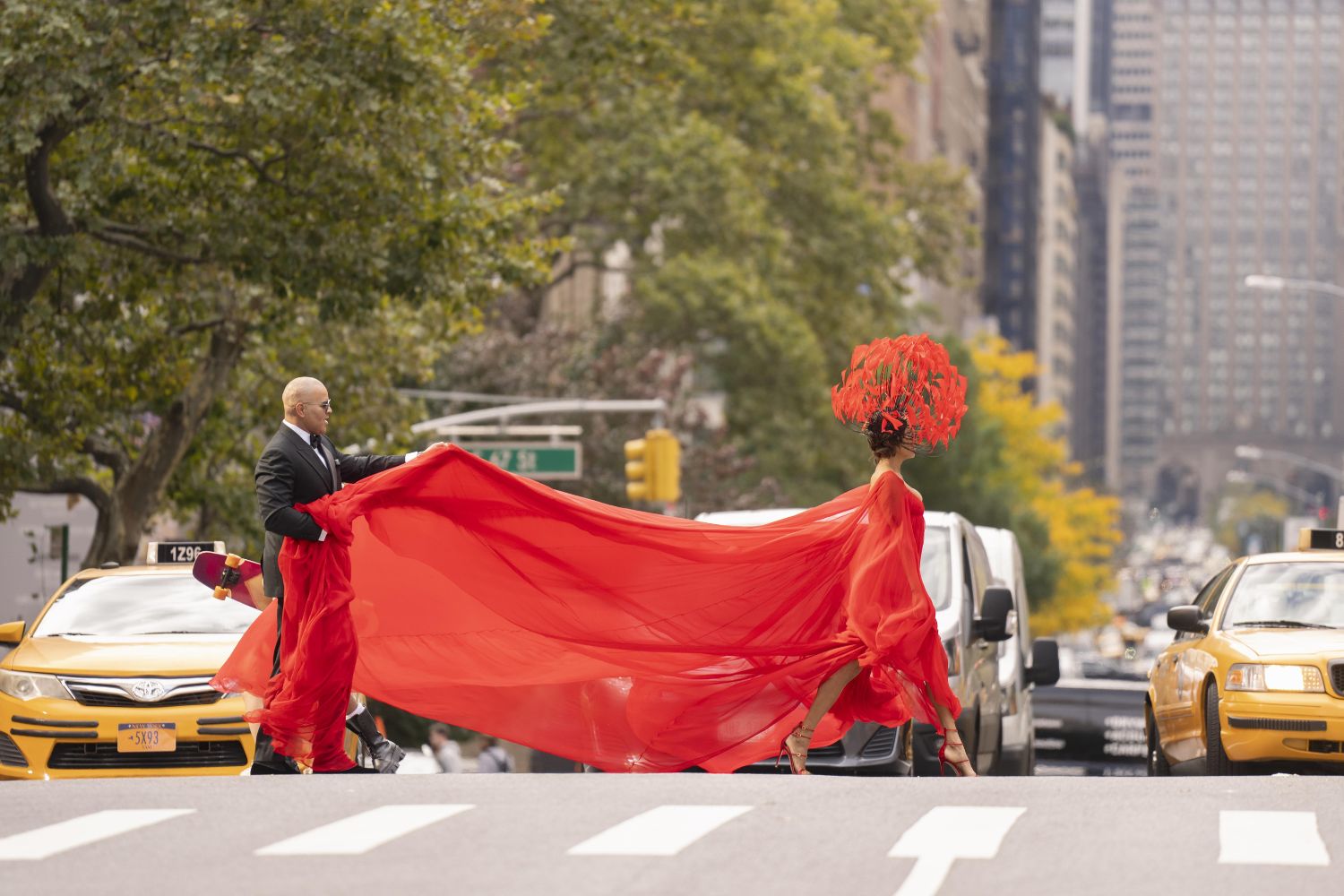Mulher atravessa uma rua de Nova York usando um vestido vermelho com longa cauda, na série "And Just Like That".