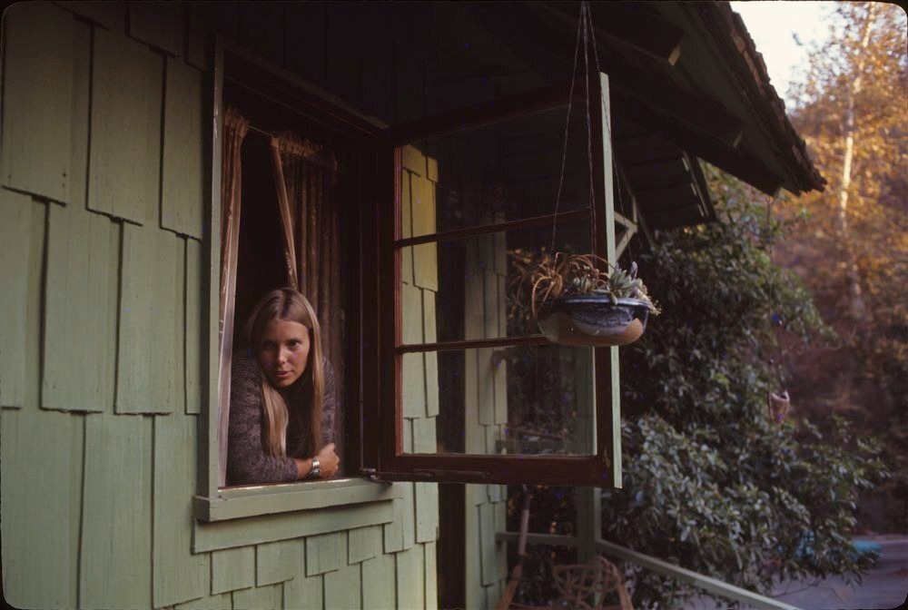 Joni Mitchell olhando pela janela de seu quarto em Laurel Canyon, em 1970. Fotógrafo Joel Bernstein.