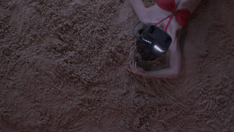 Mulher deitada no chão de areia utilizando óculos de realidade virtual