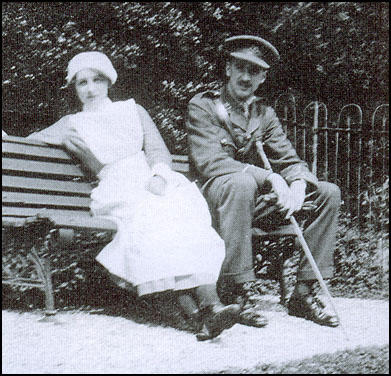 Imagem histórica de um homem e uma mulher (Vera Brittain) sentados em um banco de parque, na época antiga, em preto e branco, sugerindo um momento de descanso ou convivência ao ar livre.